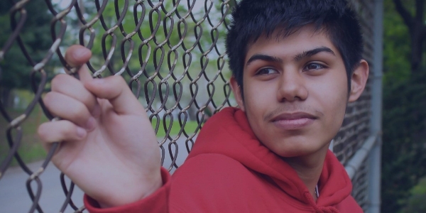 Young man in a red hoodie holding onto a chain-link fence outdoors – Elevate Project youth program in East Tulsa, Oklahoma